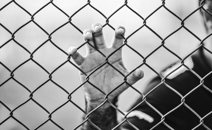 Man's hand grasping a wire prison fence